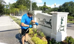 Service provider in uniform pressure washes an exterior sign for a housing development