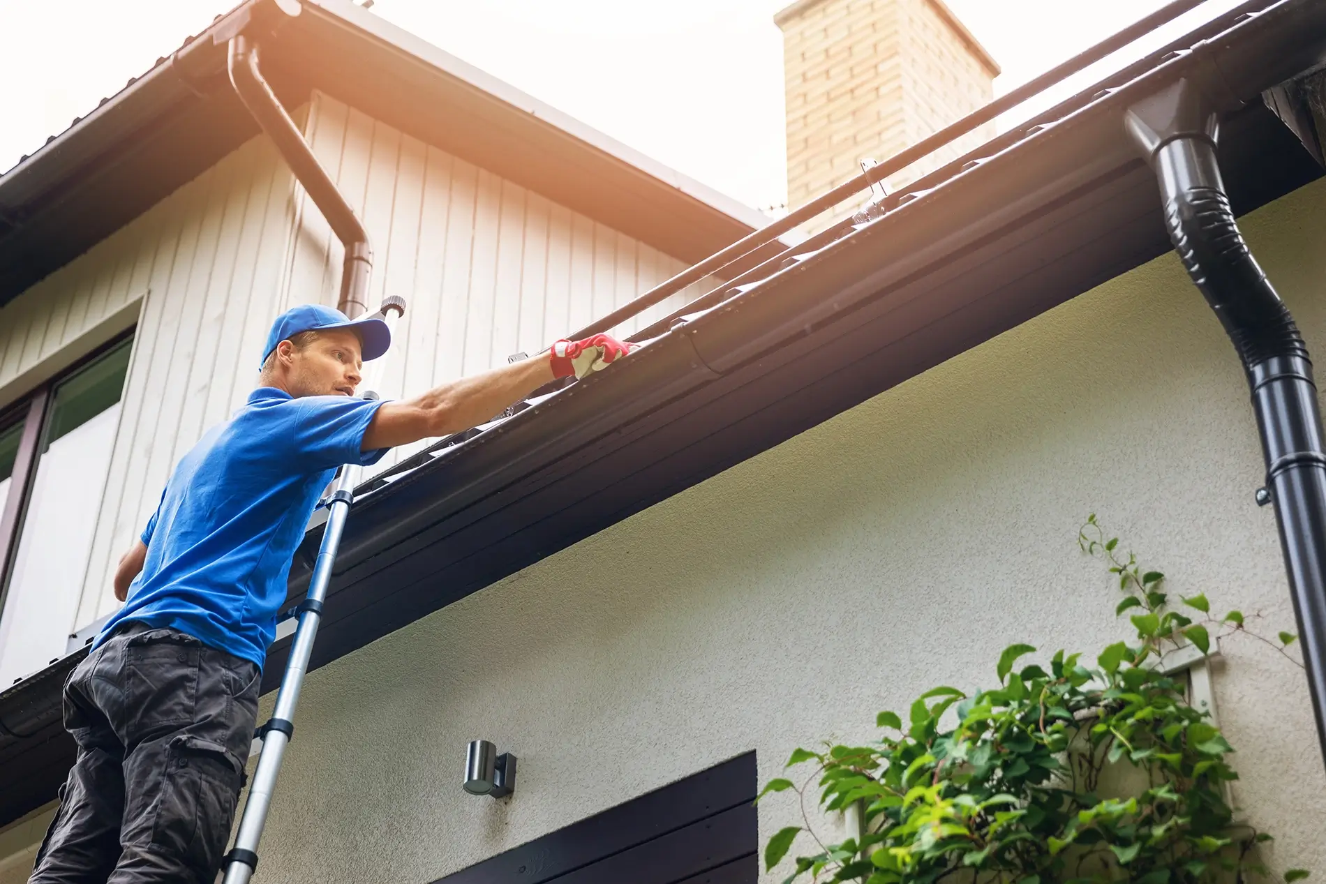 Cleaning professional stands on a ladder, carefully cleaning a roof gutter