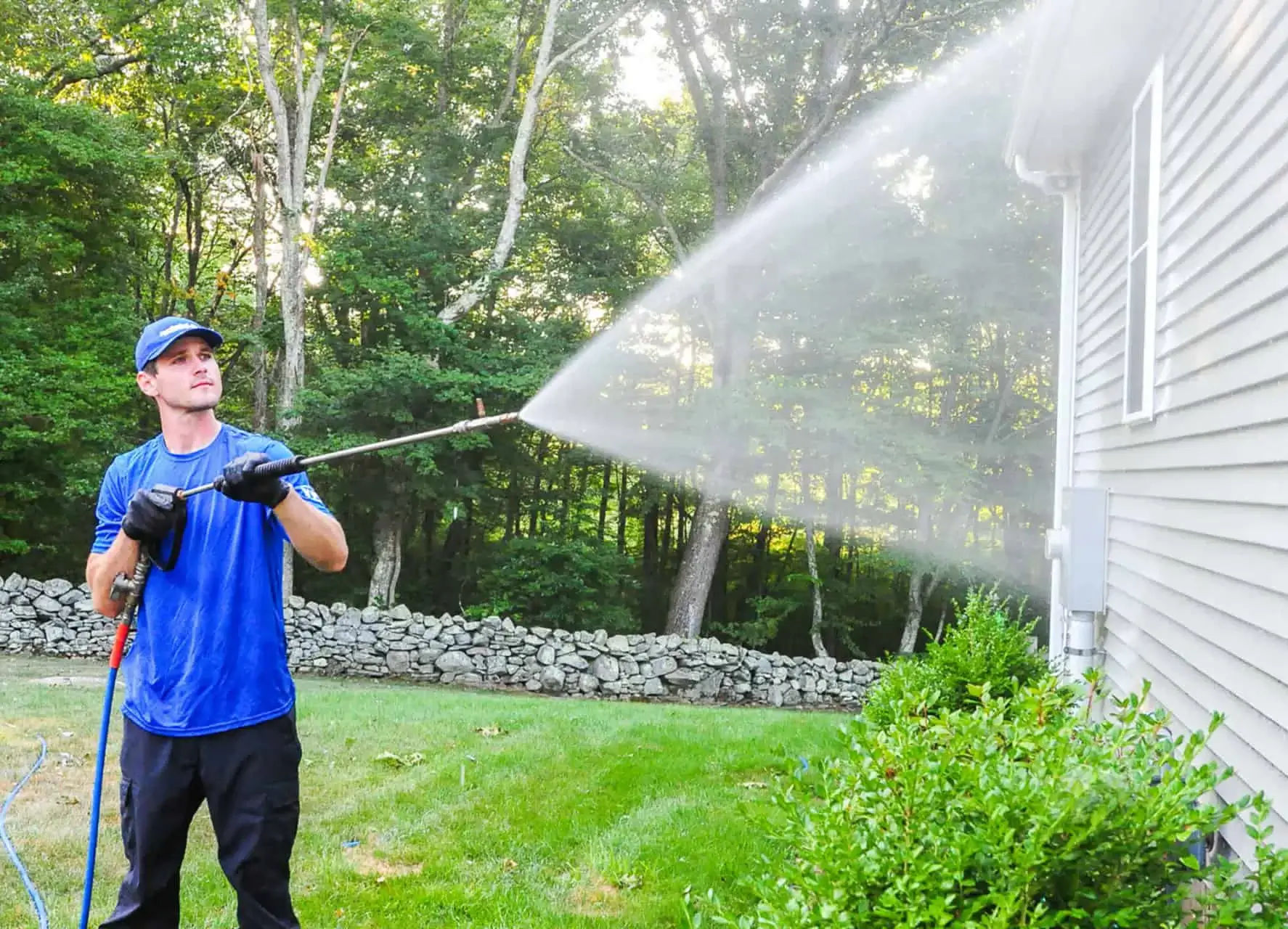 Professional in uniform, pressure washing the side of a house